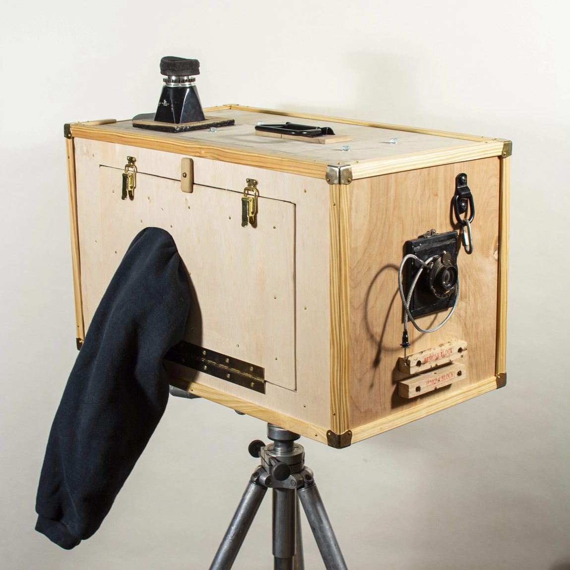The Appalachian Box Camera: a plywood box with brass corners and latches on a metal tripod, a black focusing cloth draped over the back, a shutter and viewfinder mounted on top.